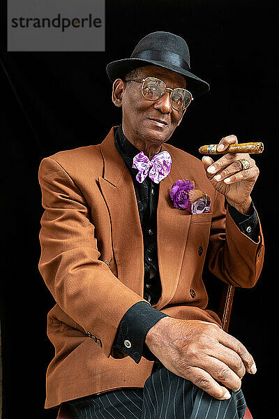 Mann sitzend  gekleidet als Dandy oder Gangster der 1950er Jahre mit Filzhut und großer Zigarre  Havanna  Kuba  Westindien  Karibik  Mittelamerika