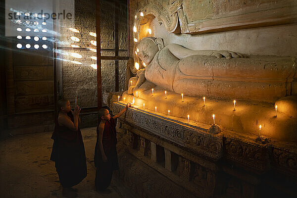 Zwei Novizenmönche zünden eine Kerze an einer buddhistischen Statue in einem Tempel an  Bagan (Pagan)  UNESCO-Weltkulturerbe  Myanmar (Burma)  Asien