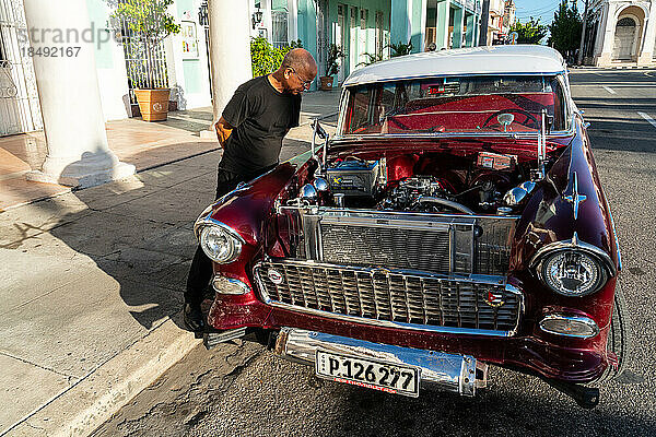Kubanischer Mann inspiziert und bewundert den offenen Motor eines roten Chevrolet-Klassikers  Cienfuegos  Kuba  Westindien  Karibik  Mittelamerika