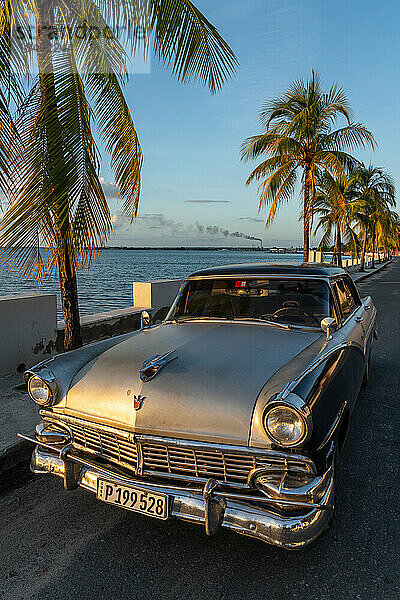 Klassischer silberner Ford auf einsamer Küstenstraße geparkt  Raffinerie im Hintergrund  Cienfuegos  Kuba  Westindien  Karibik  Mittelamerika