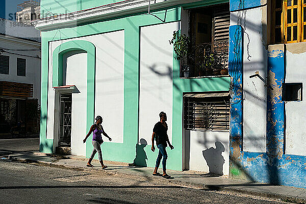 Mann und Frau und ihre Schatten  die neben bunten Gebäuden spazieren gehen  Alt-Havanna  Kuba  Westindien  Karibik  Mittelamerika