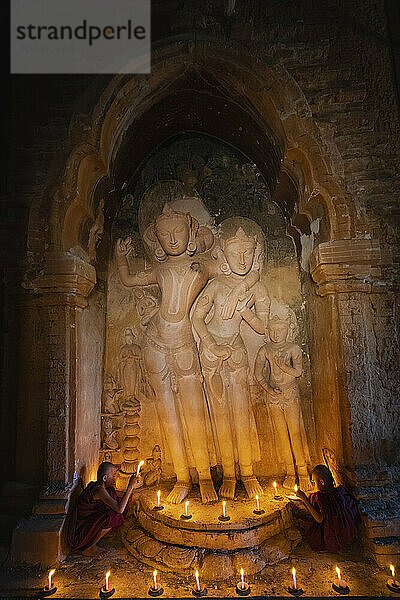 Zwei Mönchsnovizen halten Kerzen an einer Statue im Inneren eines Tempels  Bagan (Pagan)  UNESCO-Weltkulturerbe  Myanmar (Burma)  Asien