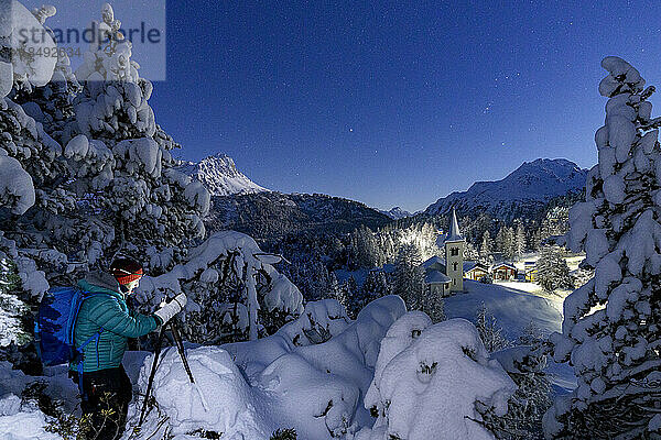 Ein Mann fotografiert die alte Chiesa Bianca bei Nacht in einem verschneiten Wald  Maloja  Engadin  Kanton Graubünden  Schweiz  Europa