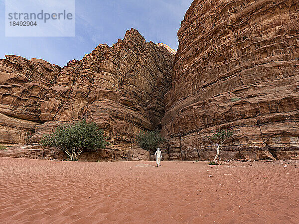 Ein Beduine in traditioneller weißer Kleidung geht in Richtung einer Schlucht in der Wüste Wadi Rum  UNESCO-Weltkulturerbe  Jordanien  Naher Osten