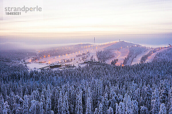 Nebel bei Sonnenuntergang über Ruka Skigebiet und verschneiten Wäldern im Winter  Luftaufnahme  Kuusamo  Nördliches Österbotten  Lappland  Finnland  Europa