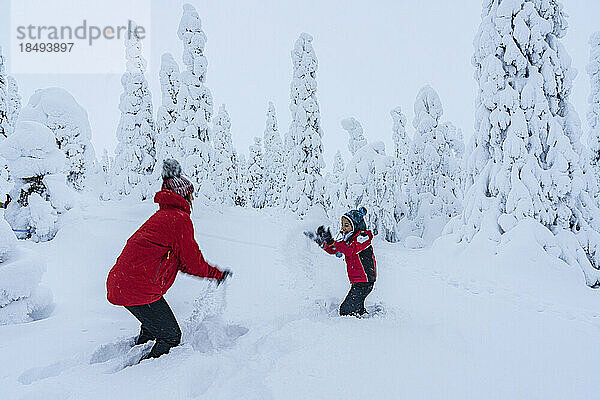 Fröhliche Mutter und Sohn genießen das Spiel mit dem Schnee in der Winterlandschaft von Finnisch-Lappland  Finnland  Europa