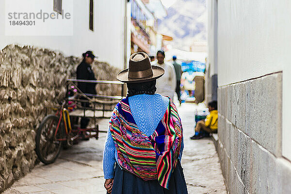 Frau  die in einer engen Straße mit einer traditionellen bunten peruanischen Tasche auf dem Rücken davonläuft  Pisaq  Peru  Südamerika
