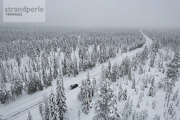 Blick von oben auf ein Auto  das auf einer vereisten Straße inmitten des gefrorenen  verschneiten Waldes fährt  Akaslompolo  Kolari  Pallas-Yllastunturi-Nationalpark  Region Lappland  Finnland  Europa
