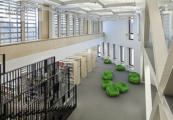 Eine Universitätsbibliothek für das Gesundheitswesen mit Freiflächen  grünen Stühlen und Bücherstapeln. Ein modernes  helles und luftiges Gebäude.