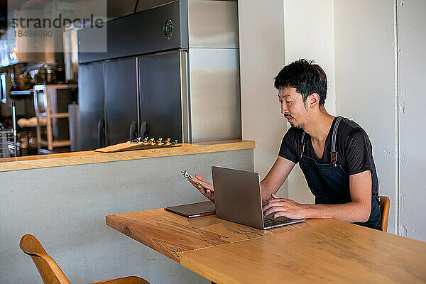 Ein Mann  der mit einem Laptop an einem Tisch sitzt  Besitzer und Manager eines kleinen Restaurants.