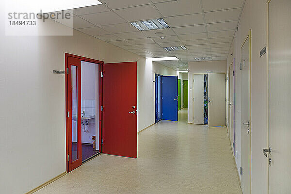 Ein Schulkorridor mit farbigen Türen  die davon abgehen. Rote  blaue und grüne Türen. Schließfächer und Schränke.