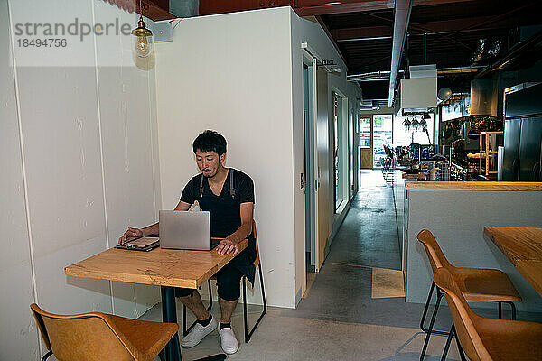 Ein Mann  der mit einem Laptop an einem Tisch sitzt  Besitzer und Manager eines kleinen Restaurants.