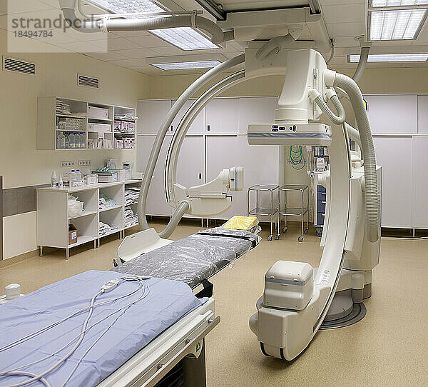 Ein modernes Krankenzimmer  ein großes tragbares mobiles Scangerät mit gebogenen Armen  ein mobiler Scanner und eine Krankenliege oder ein Krankenhausbett.