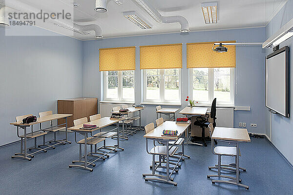 Ein Schulklassenzimmer mit Schreibtischen und Stühlen und gelben Jalousien.