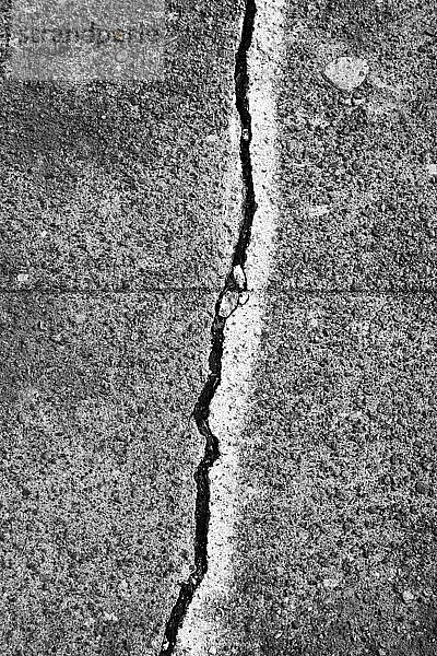 Ein Riss zwischen mit einer weißen Linie bemalten Steinplatten auf einer Betonoberfläche des Gehwegs.