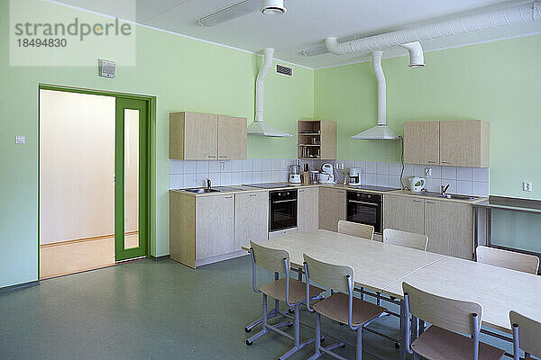 Eine moderne Schule  eine Küche mit Einbauschränken und Öfen  ein langer Tisch und Stühle.