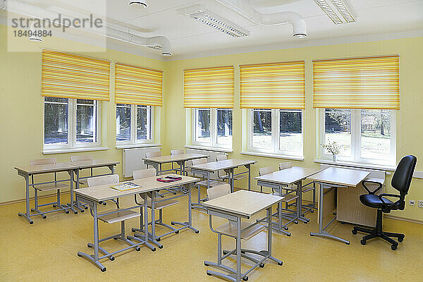 Ein Schulklassenzimmer mit Schreibtischen und Stühlen und gelben Jalousien.