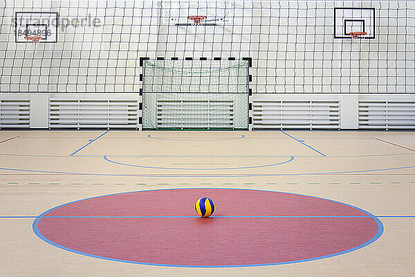 Eine Schulsporthalle mit einem markierten Hallenfußballfeld  Tor und Basketballkörben  einem gestreiften blau-gelben Ball in einem rosa Kreis.