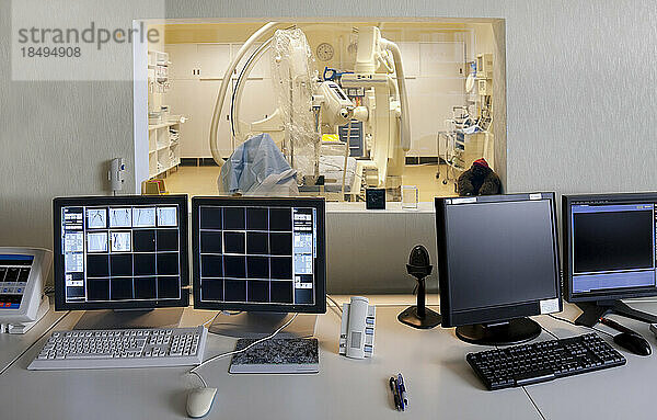 Ein modernes Krankenzimmer  ein großes tragbares mobiles Scangerät mit gebogenen Armen und Bildschirmreihen für die medizinische Bildgebung  Blick aus dem Kontrollraum.