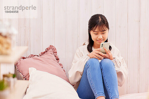 Japanisches Mädchen mit Smartphone im Bett