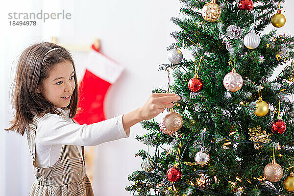 Lächelndes junges Mädchen  das Weihnachtsbaum schmückt