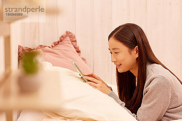 Japanisches Mädchen mit Smartphone im Bett