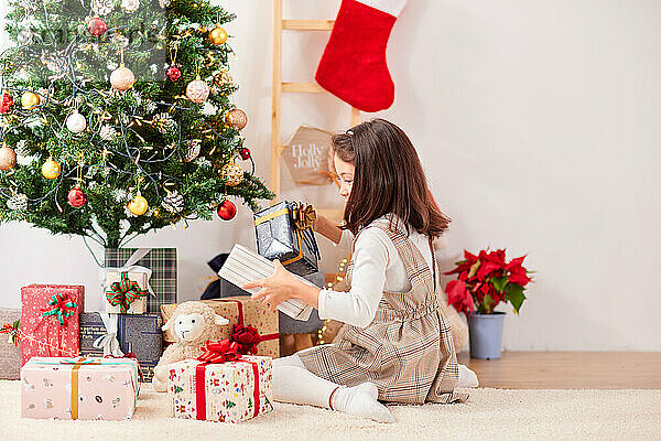 Lächelndes junges Mädchen  das Weihnachtsgeschenke öffnet