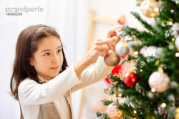 Lächelndes junges Mädchen  das Weihnachtsbaum schmückt