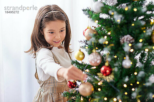 Lächelndes junges Mädchen  das Weihnachtsbaum schmückt