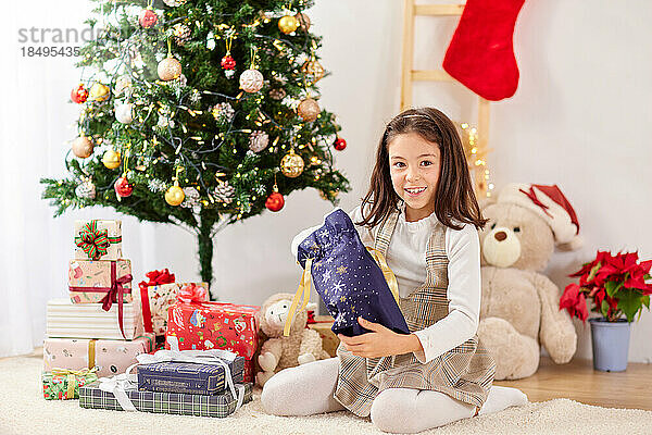 Lächelndes junges Mädchen  das Weihnachtsgeschenke öffnet