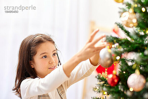 Lächelndes junges Mädchen  das Weihnachtsbaum schmückt