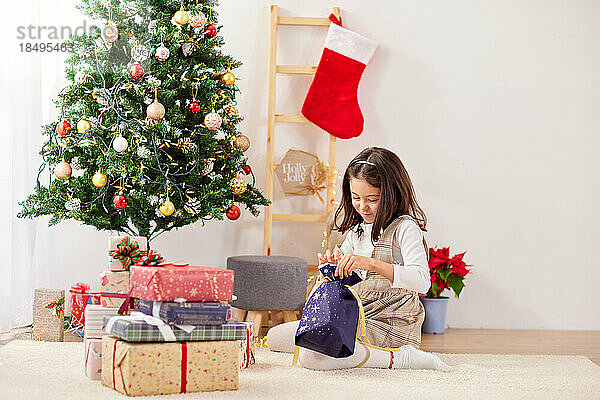 Lächelndes junges Mädchen  das Weihnachtsgeschenke öffnet