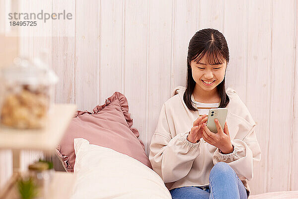 Japanisches Mädchen mit Smartphone im Bett