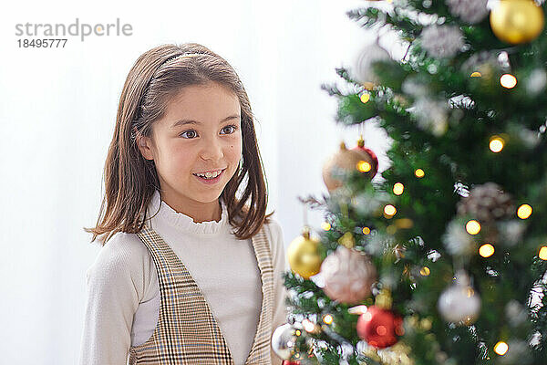 Lächelndes junges Mädchen  das Weihnachtsbaum schmückt