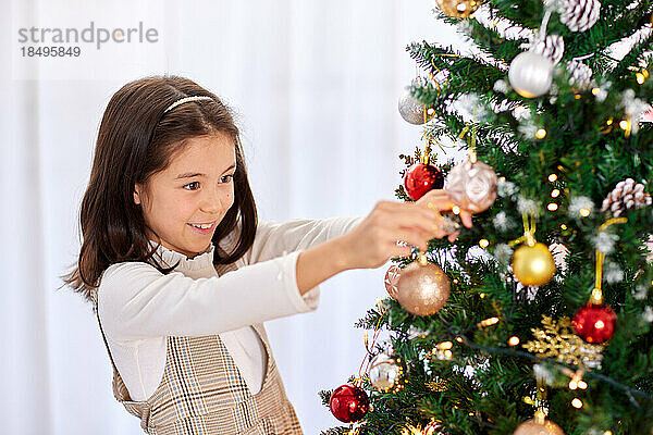 Lächelndes junges Mädchen  das Weihnachtsbaum schmückt