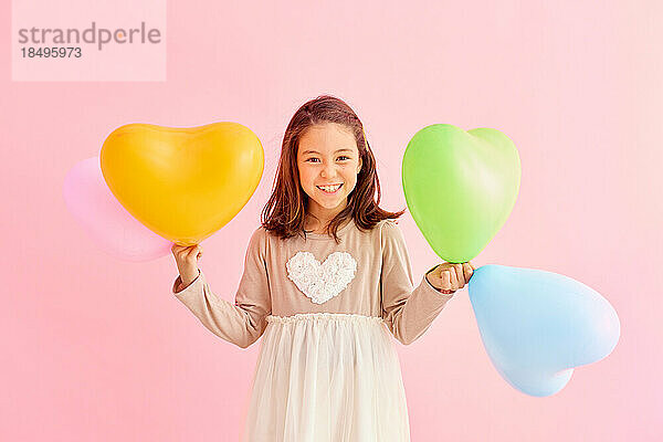 Smiling young girl holding heart balloons