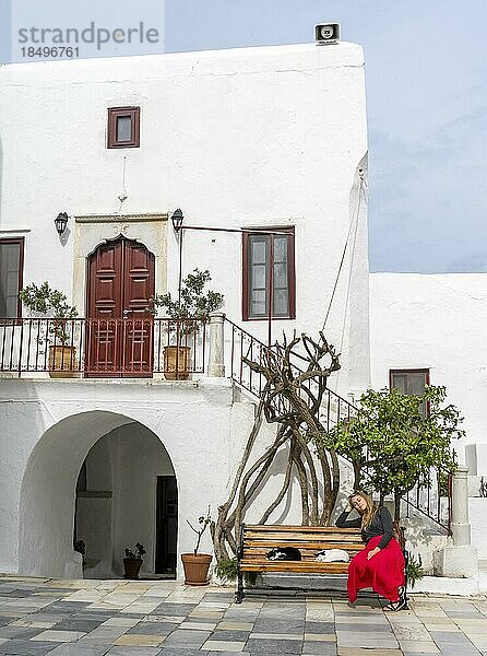 Junge Frau mit rotem Rock sitzt auf einer Bank mit schlafenden Katzen  Kykladische weiße Häuser  Kloster Panagia Tourliani  Ano Mera  Mykonos  Kykladen  Griechenland  Europa