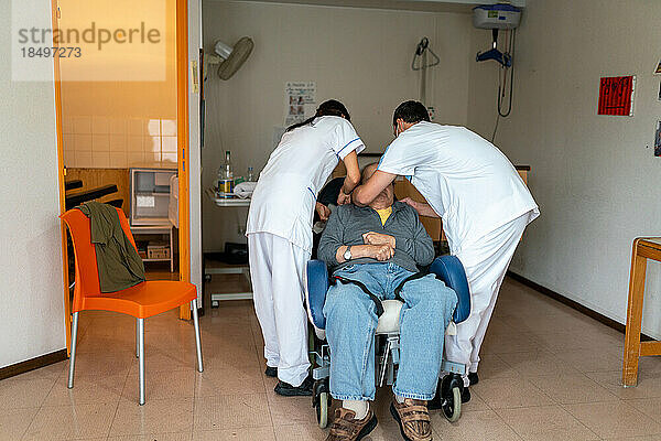 Zwei Pflegehelferinnen bringen eine behinderte Patientin in ihrem Zimmer im Pflegeheim zu Bett.