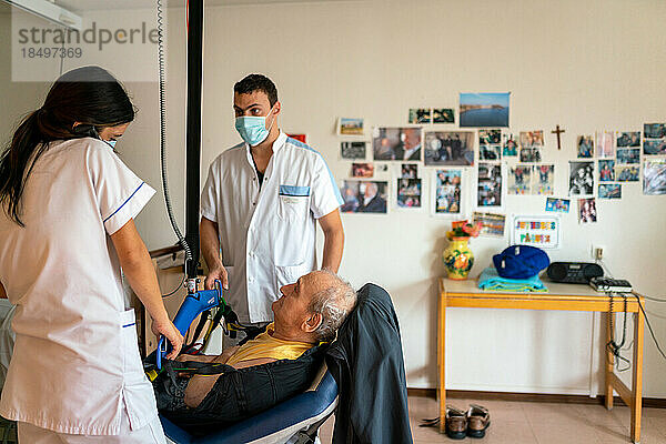 Zwei Pflegehelferinnen bringen eine behinderte Patientin in ihrem Zimmer im Pflegeheim zu Bett.