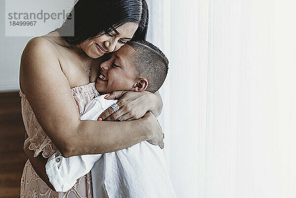 Seitenansicht einer Mutter und ihres kleinen Sohnes  die sich im Studio mit natürlichem Licht umarmen