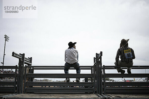 Fast silhouettierte Cowboys sitzen auf einem Zaun beim Arizona Black Rodeo