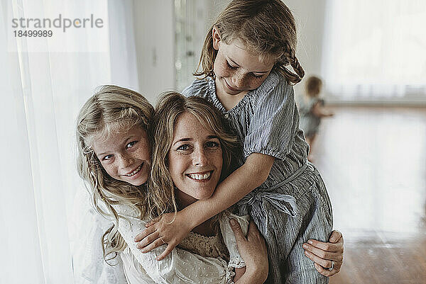 Töchter umarmen lächelnde Mutter im Studio mit natürlichem Licht