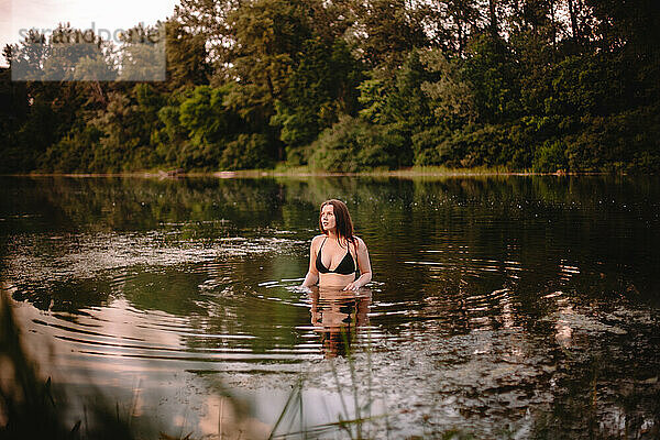 Junge Frau steht im See vor Bäumen