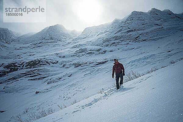 Mann geht vor einem dramatisch verschneiten Bergrücken