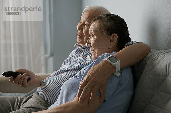 Älteres Paar schaut zu Hause fern und nutzt die Fernbedienung