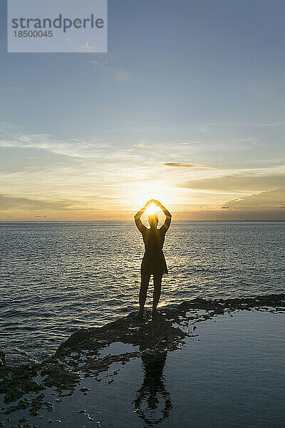 Silhouette einer Frau  die bei Sonnenuntergang am Strand von Nusa Lembongang  Bali  Indonesien  gegen die Sonne gestikuliert