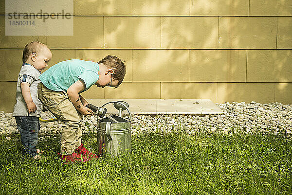 Zwei kleine Jungen im Garten füllen Gießkanne