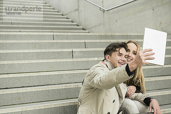 Junges Paar sitzt auf einer Treppe und macht ein Selfie mit einem digitalen Tablet  München  Bayern  Deutschland