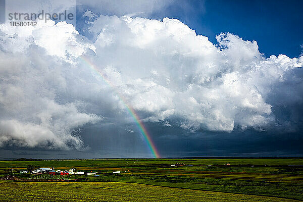Regenbogen und weiße schwere Wolken über Bauernhof und grünen Feldern