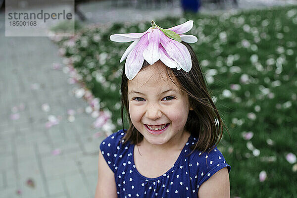 A giggling little girl wears a magnolia blossom for a hat